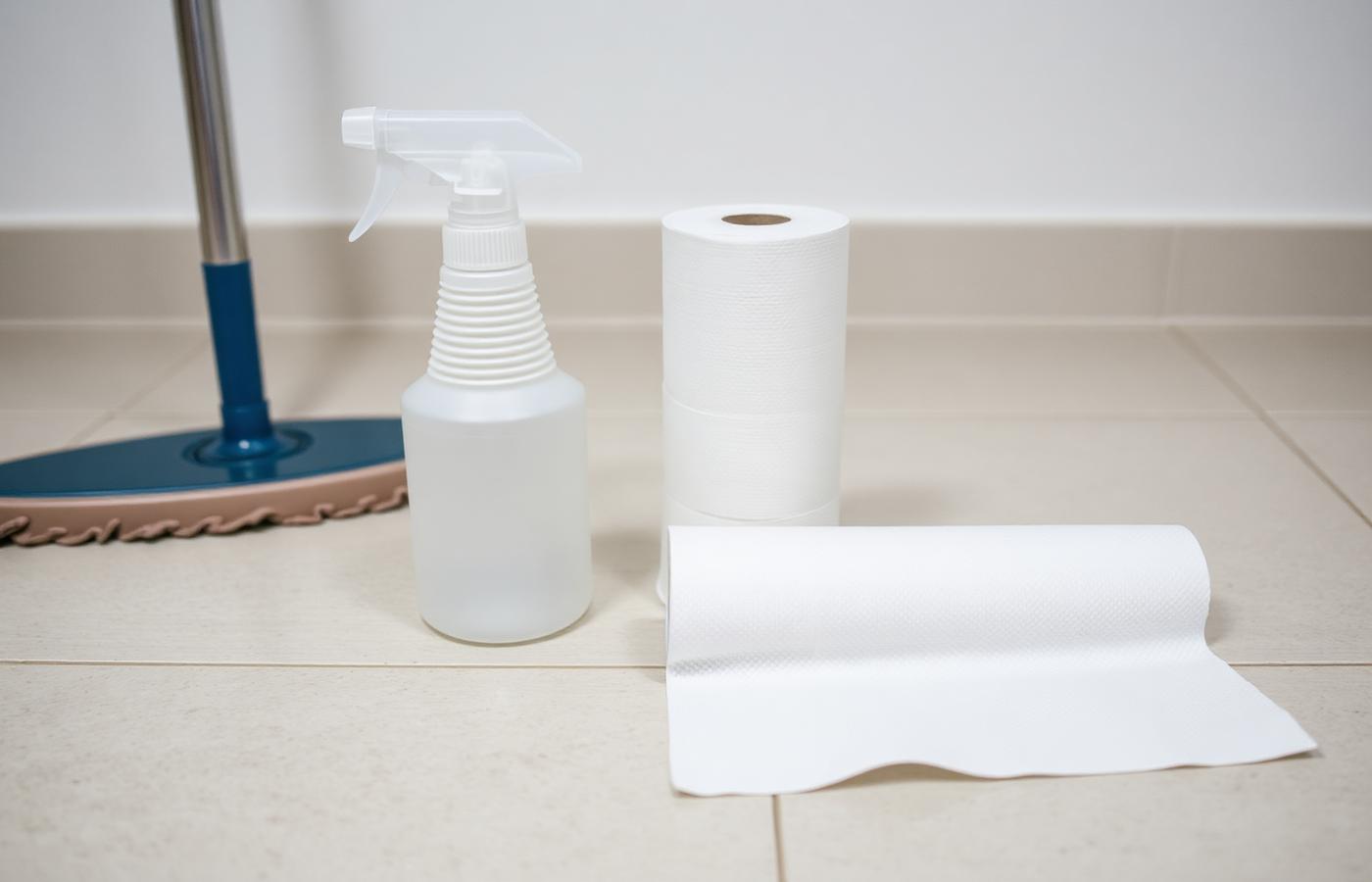 Plain spray bottle and paper towels on a clean tile floor next to a mop